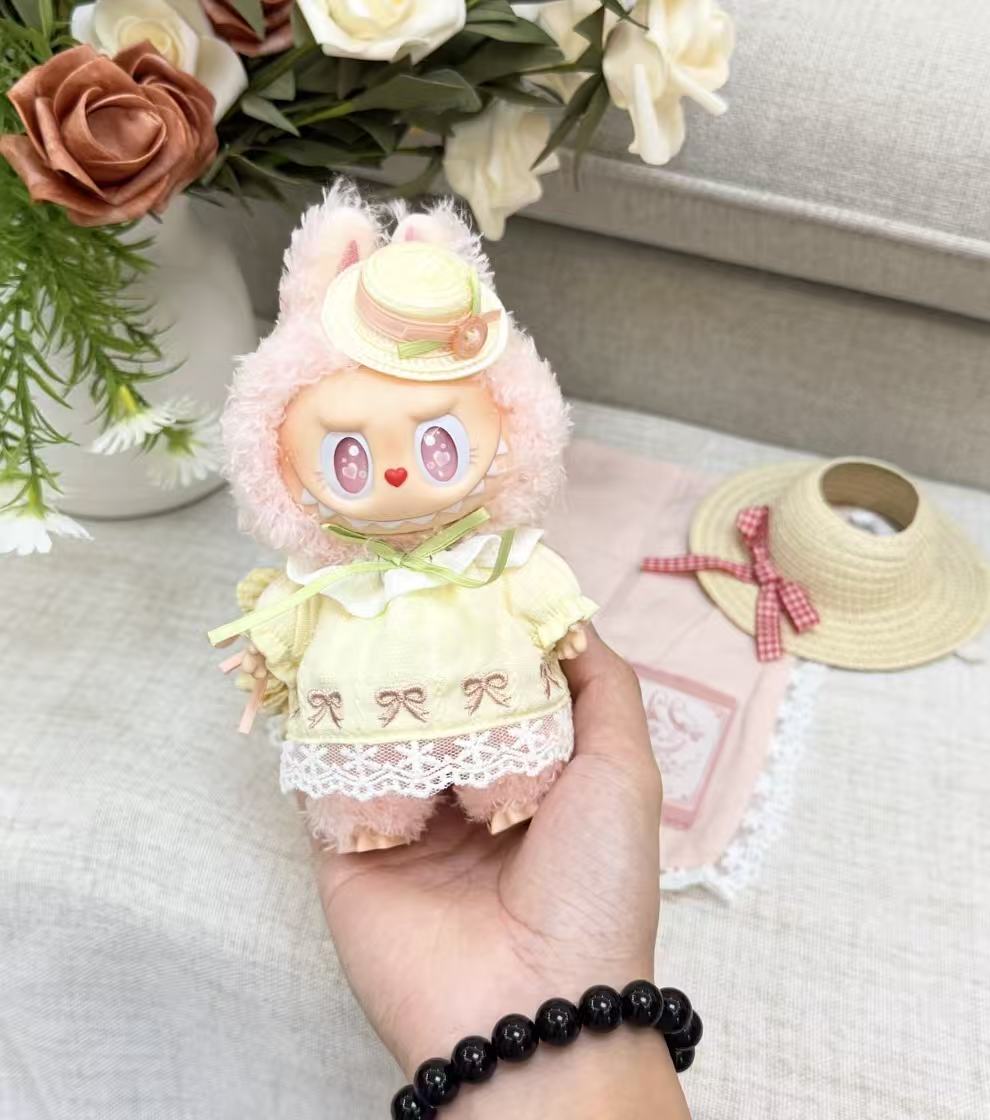 Handheld close-up of POP MART MOKOKO plush pendant showing the yellow embroidered dress, lace hem and straw-style hat