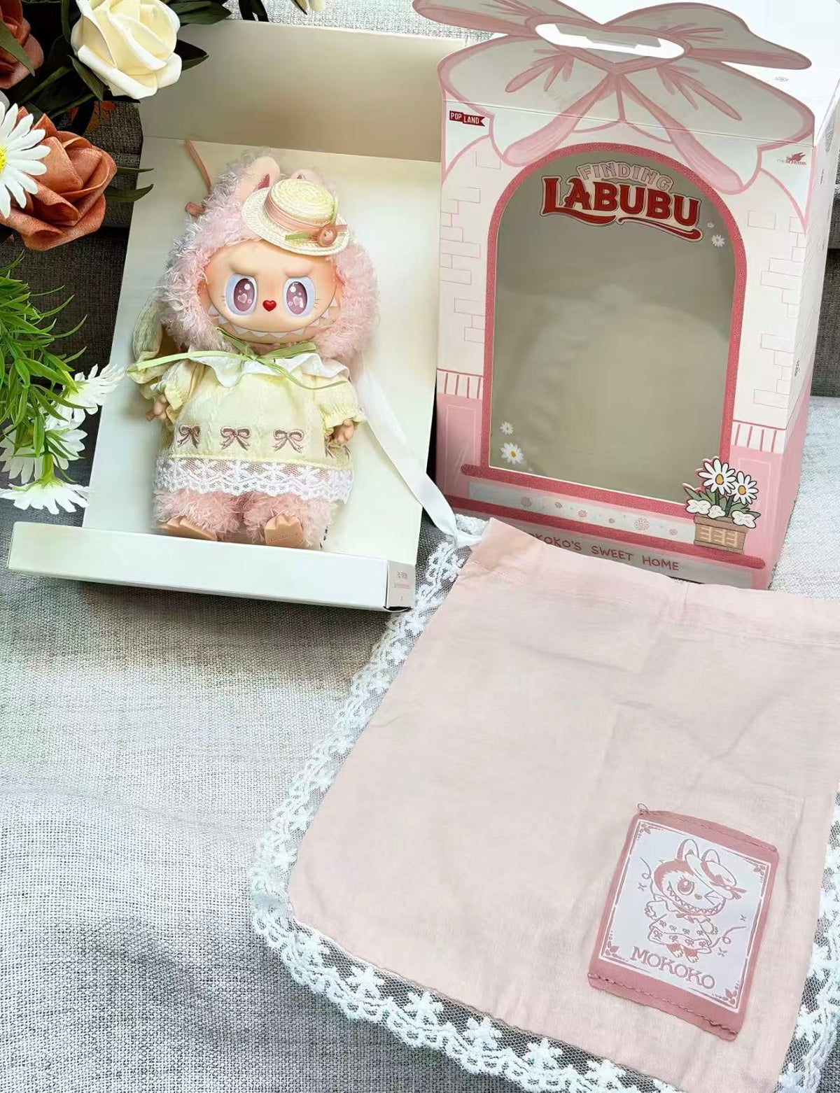 POP MART MOKOKO yellow-dress plush pendant displayed beside pink Finding Labubu packaging and a MOKOKO fabric pouch